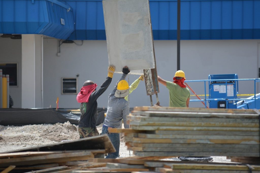 Three construction workers hold up construction material on work site.