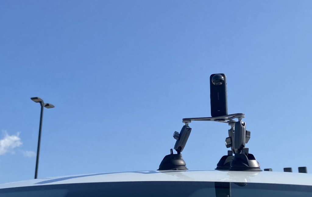 Camera mounted with tripod on top of vehicle surface. Blue background.